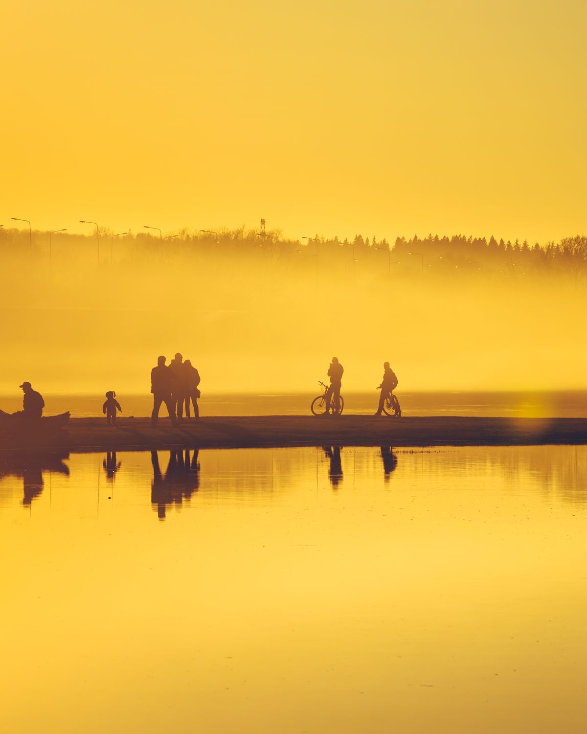 People on a causeway across still water at golden hour, seen from above