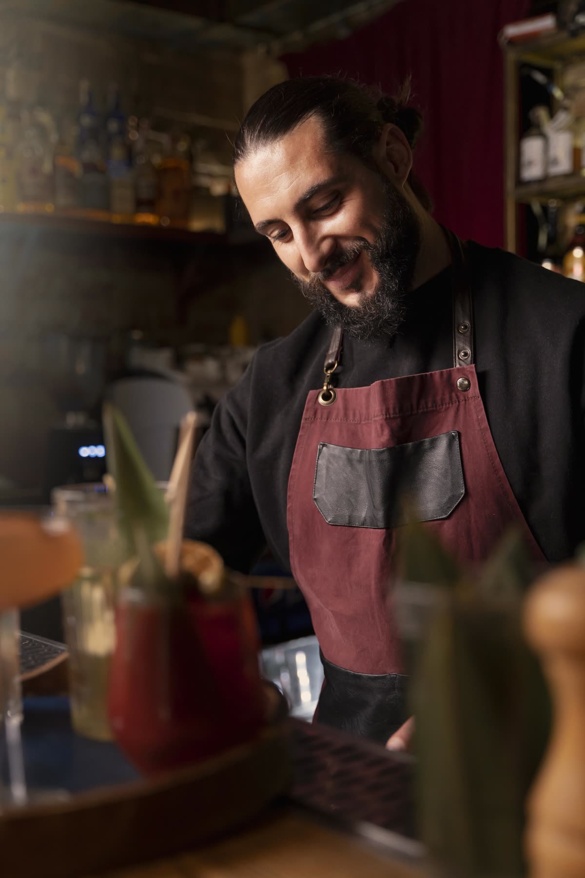 A bartender making a drink behind a dark bar