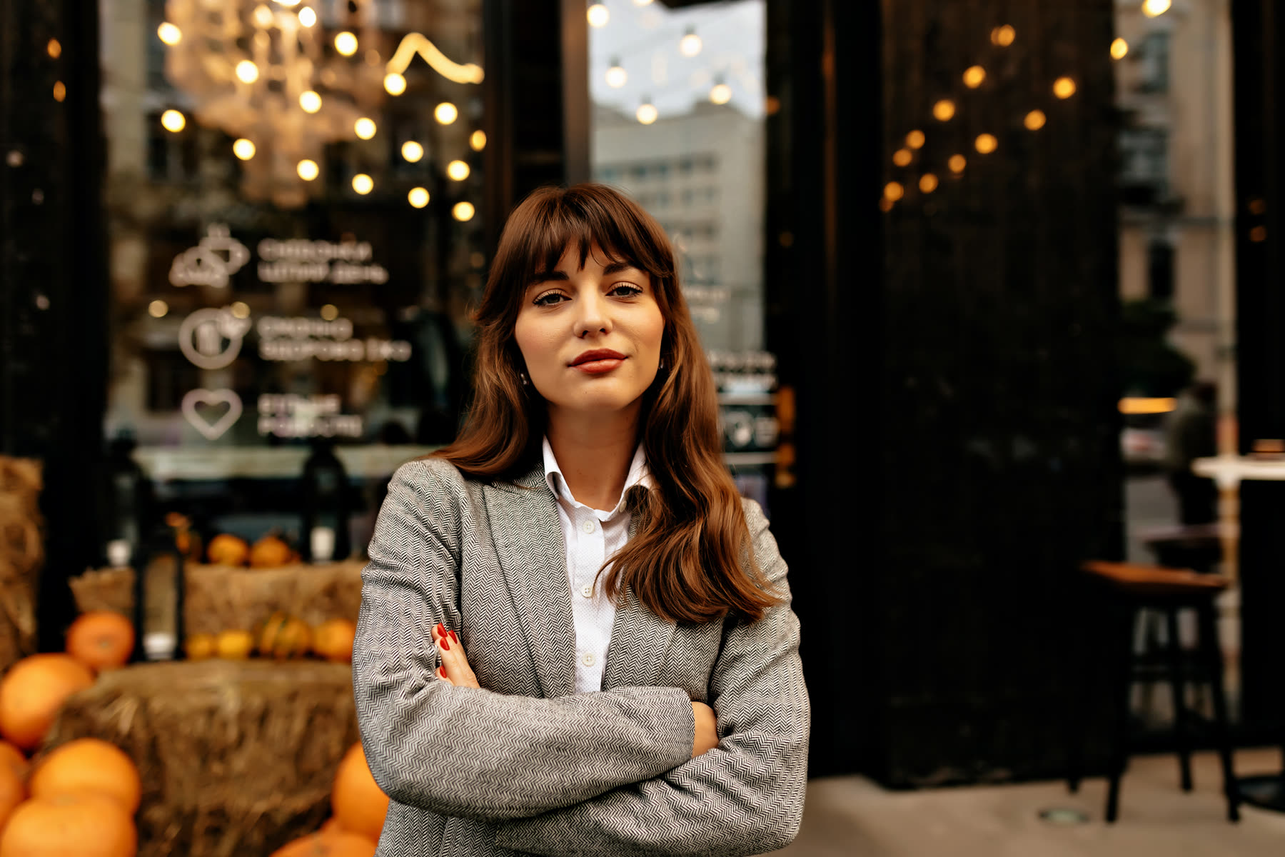 A woman in a blazer standing outside her business, arms folded