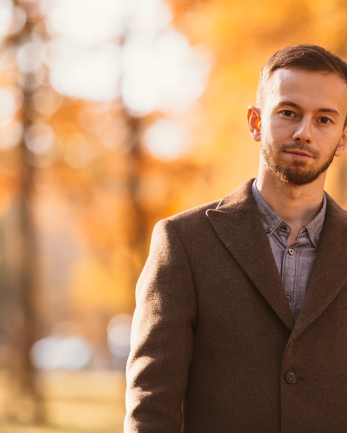 A man in a wool jacket outdoors against autumn leaves