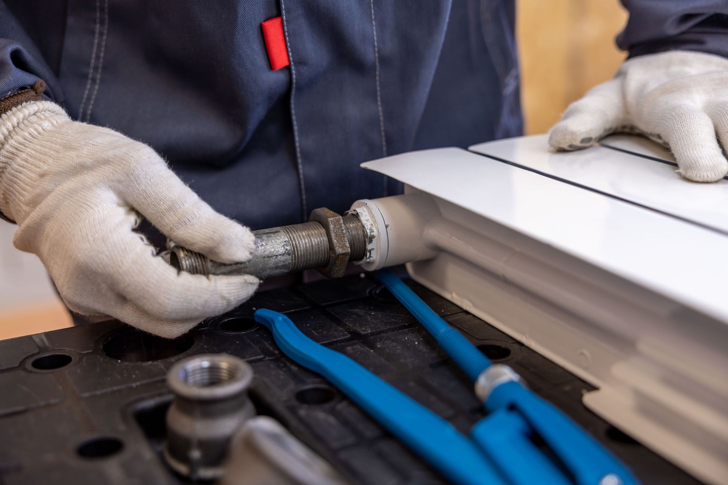 Gloved hands fitting a pipe into a radiator on a workbench