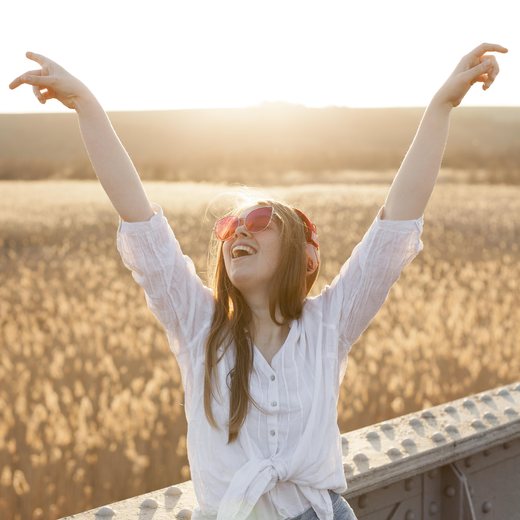 A woman standing in a field at sunrise with her arms thrown up