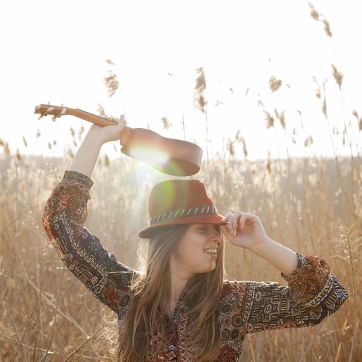 A woman playing a ukulele in tall grass, backlit by the sun