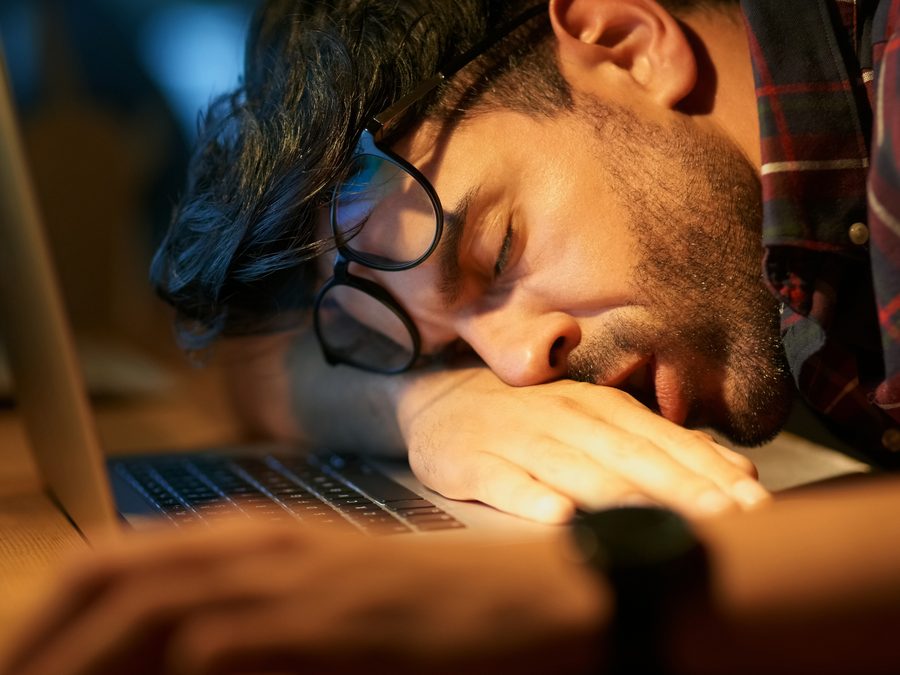 A man asleep at his desk beside an open laptop
